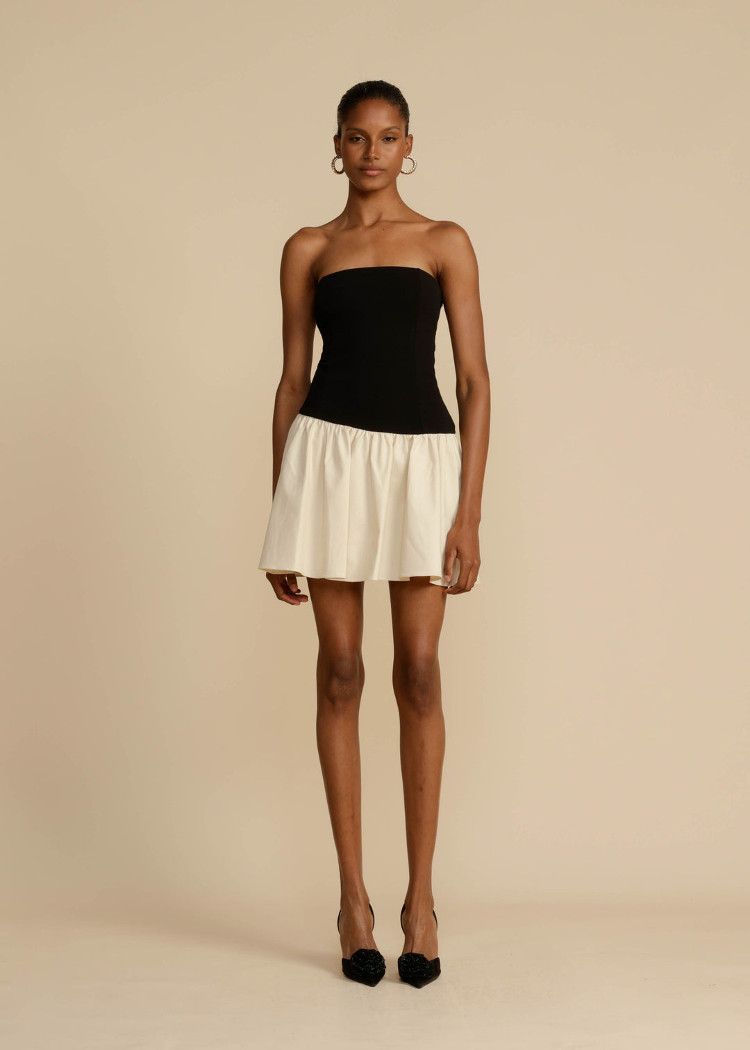 Woman wearing a black strapless top and white skirt on a beige background