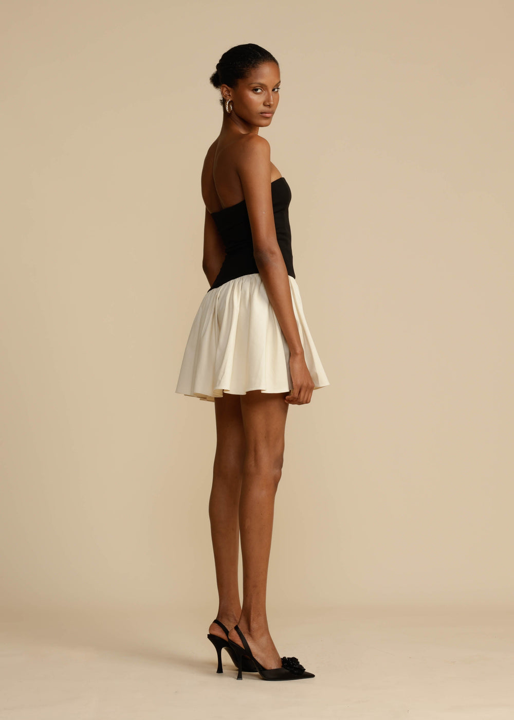 Woman wearing a black strapless top and white skirt on a beige background