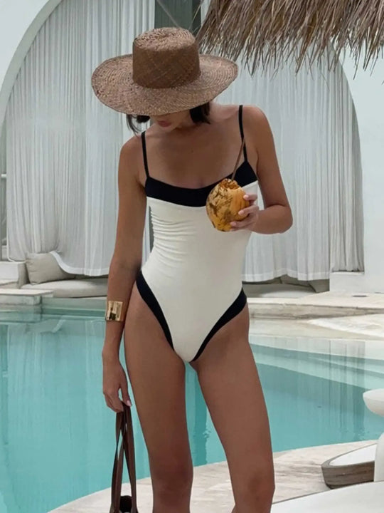 Woman in a white and black swimsuit with a straw hat by a pool.