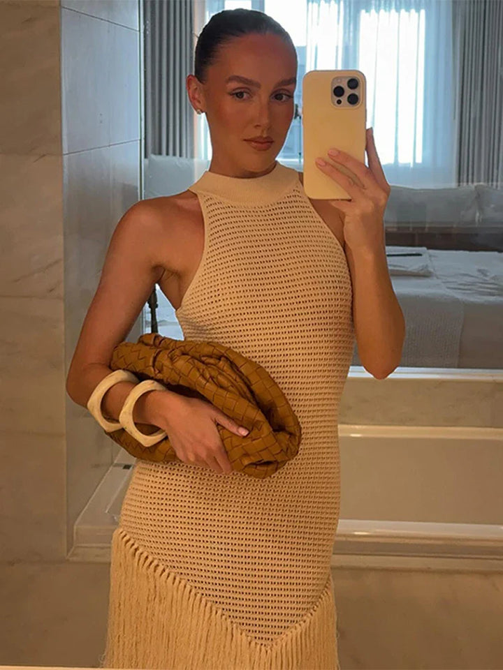 Woman taking a mirror selfie wearing a beige knit dress and holding a brown clutch.